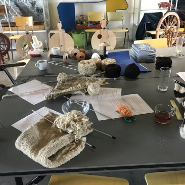 Tafel met breiwerkjes, op de achtergrond staan spinnewielen