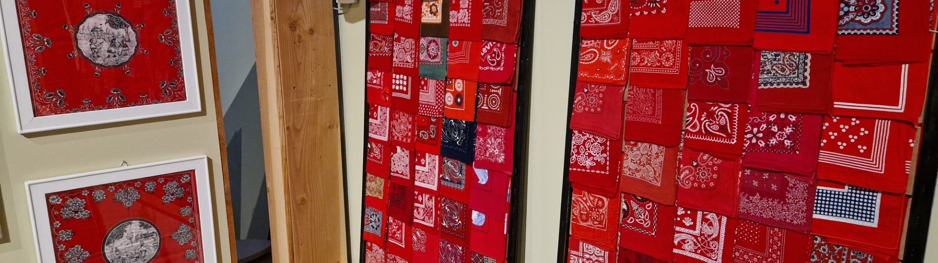 Een deel van de tijdelijke expositie van de rode boerenzakdoek in het Fries Landbouwmuseum. Links hangen twee zakdoeken in een lijst, aan de rechterkant zijn twee panelen te zien met een verzameling van zakdoeken erop.